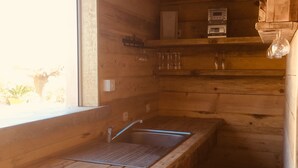Un intérieur en bois avec un coin cuisine comprenant un évier, une fenêtre et une étagère où sont rangés les appareils de cuisine.