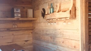 L’intérieur d’un chalet en bois comprend un coin cuisine équipé d’un évier, d’un four à micro-ondes et d’une étagère où sont rangées des bouteilles et des verres.
