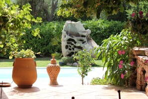 A garden with a stone sculpture, potted plants, and a tiled patio area. - VILLA CLIMATISEE WITH PRIVATE SWIMMING POOL (Porto-Vecchio)