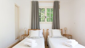 Hotellihuone, jossa on kaksi sänkyä, ikkuna, jossa on verhot, ja yöpöydällä olevat lamput.