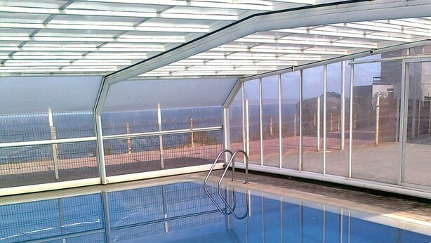 En indendørs swimmingpool med glasvægge, et metalgelænder og flisegulv.