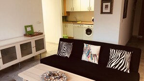 En moderne stue med en sort sofa, et træbord og et køkken i baggrunden.