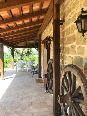 Eine überdachte Terrasse mit Steinmauern, Holzbalken und Gartenmöbeln.