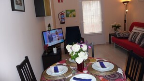 A dining area with a round table set for four, a television displaying a news program, a fire extinguisher, and a door labeled "SALIDA". - APARTMENT FOR 4 PEOPLE IN LIENCRES (Liencres)