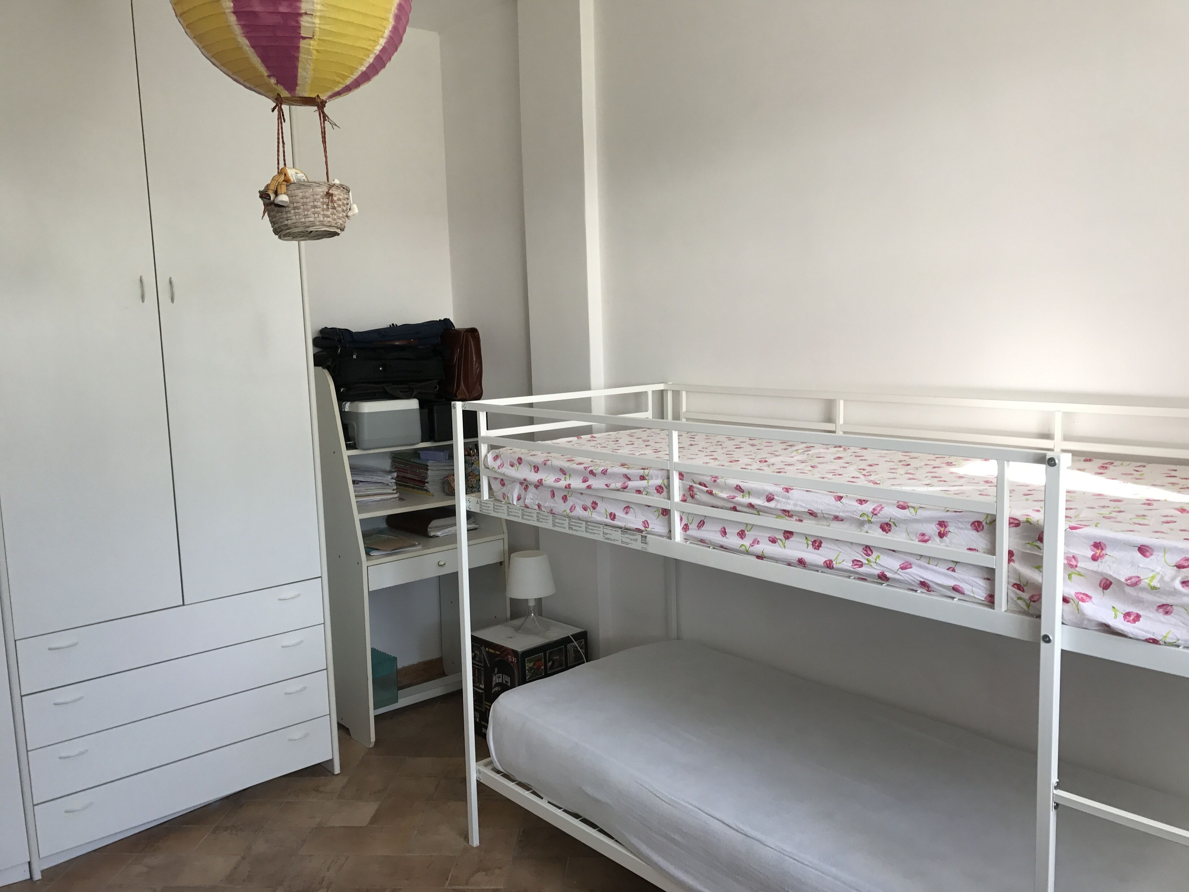 Un lit superposé avec une couvre-lit à motifs floraux, une armoire blanche et un bureau avec une lampe et des boîtes de rangement.