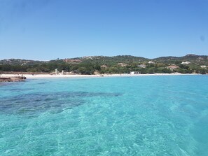 Une vue sur la côte, avec une eau turquoise cristalline, une plage de sable et des bâtiments situés sur une colline en arrière-plan.