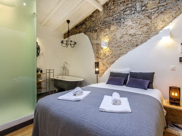 A bedroom with a stone wall, a bathtub, and a bed with towels.