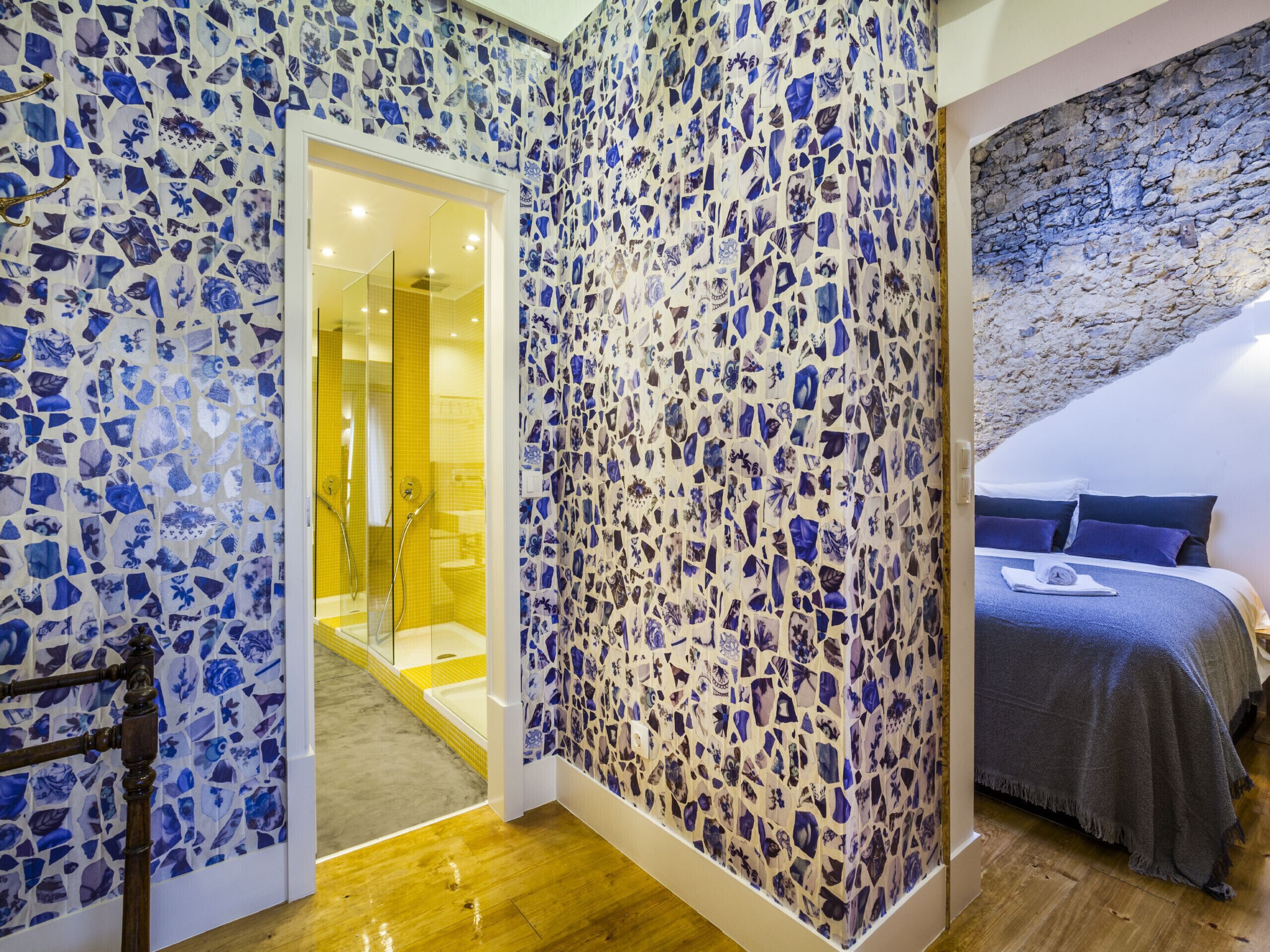 Una habitación con pared de mosaicos, suelo de madera, cama con colcha azul y pared de piedra.