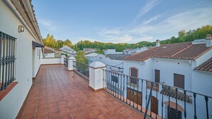 Una terraza en la azotea con baldosas de terracota, paredes blancas y techos de tejas rojas.