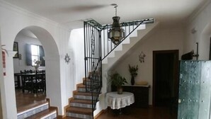 Una escalera con barandilla de metal que lleva a una plataforma, una mesa redonda con una planta y un suelo de madera.