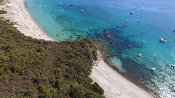 An aerial view of a coastal area with a sandy beach, clear blue waters, and scattered boats. - 2-bedroom apartment on beach, sea and marina view, air-conditioned & WiFi Fiber. (Propriano)