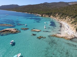 A coastal area with clear turquoise waters, rocky outcrops, and a sandy beach with people and boats.
