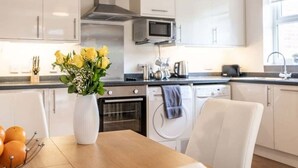 A modern kitchen with white cabinets, a microwave, and a sink. There is a vase with yellow flowers on the table.