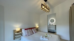 A modern hotel room with a neatly made bed, a bedside lamp, a mirror, and a unique geometric light fixture. - Stone house in Luberon, heated infinity pool, patio, near Gordes (Murs)