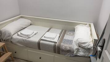 Una cama individual con colcha blanca, dos almohadas y toallas dobladas.