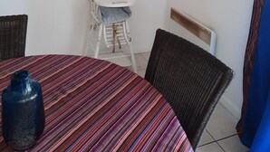 Een kamer met een gestreept beddegoed, een kinderstoel, twee ingelijste kunstwerken en een rieten stoel.