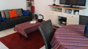 Een woonkamer met een bank, salontafel, televisie en een eethoek met tafel en stoelen.