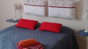 Een slaapkamer met een bed, twee kussens, een deken, een lamp en een spiegel aan de muur.