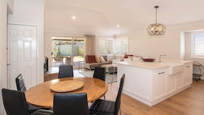 Una cocina moderna con una isla central, un comedor con una mesa redonda de madera y una sala de estar con un sofá y sillones.