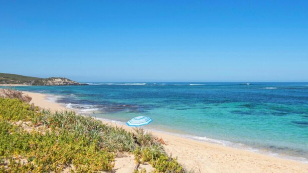 Una playa con agua turquesa cristalina, orilla arenosa y vegetación verde.