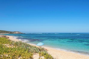 A beach with clear turquoise water, sandy shore, and green vegetation.