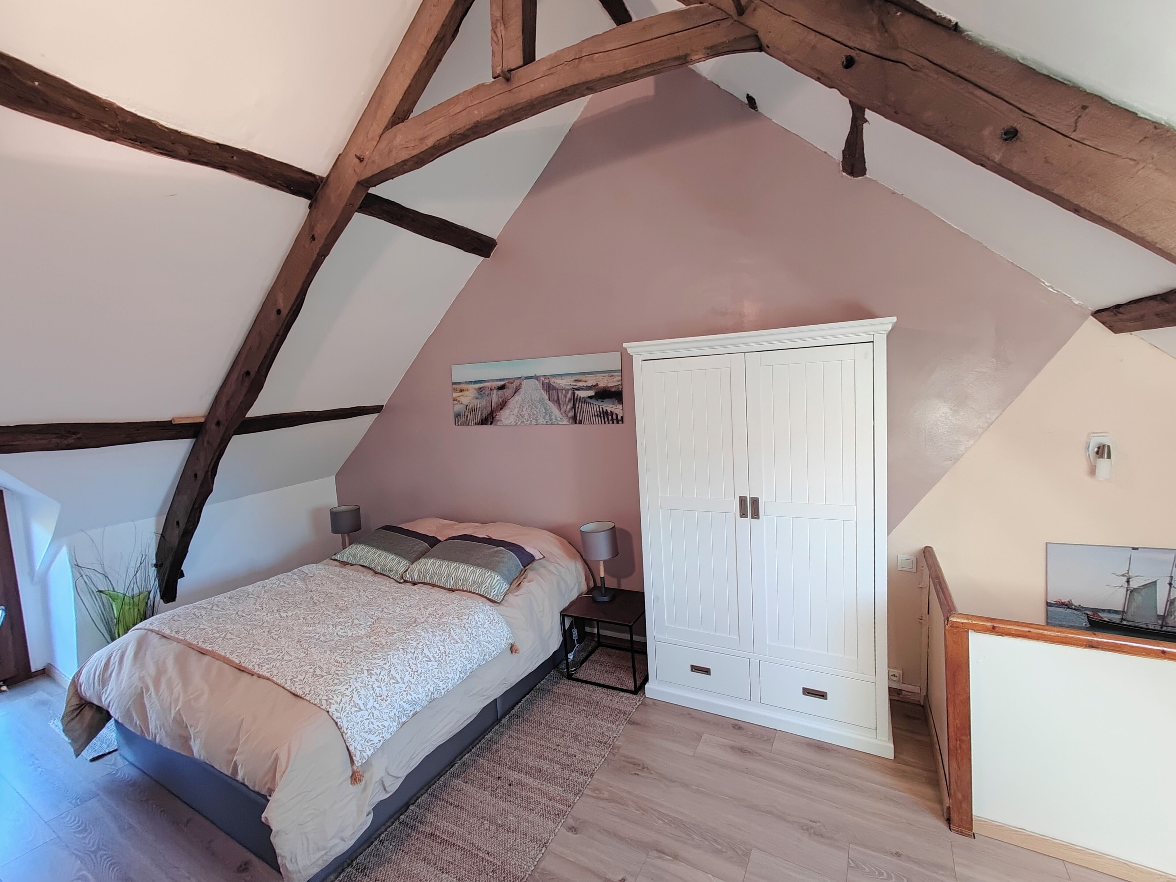 A bedroom with a sloped ceiling, a bed with a patterned bedspread, a wardrobe, and a painting on the wall.