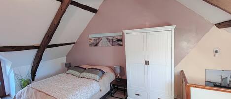 A bedroom with a sloped ceiling, a bed with a patterned bedspread, a wardrobe, and a painting on the wall.