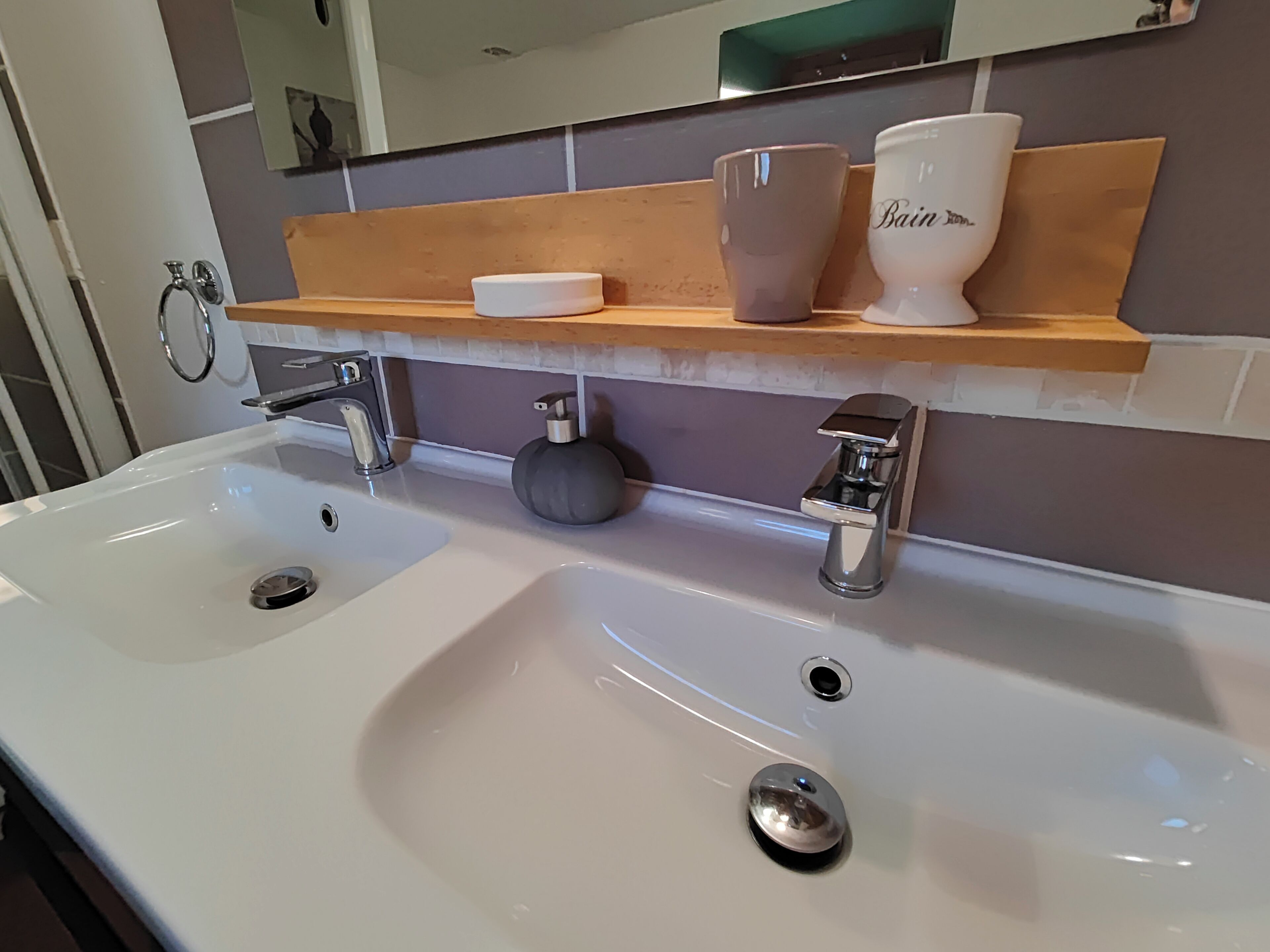 Un baño con un lavabo blanco, dos llaves, un dispensador de jabón y un estante con una taza y un recipiente.