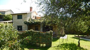 Une maison en pierre avec un jardin, un petit arbre et une pelouse.