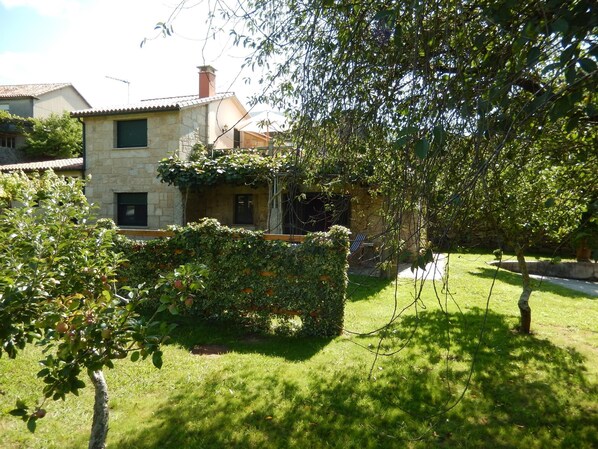 A stone house with a garden, a small tree, and a grassy lawn.