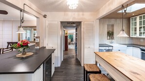 A modern kitchen with a central island, wooden bench, pendant lighting, and a view into the dining area.