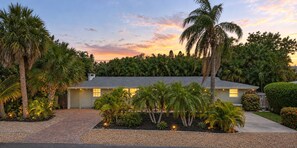 A single-story house with a paved driveway, surrounded by palm trees and a well-maintained garden. - Twin Palms: Big House Close to Beach, Heated Lagoon Pool, Infant/Pet friendly (Holmes Beach)