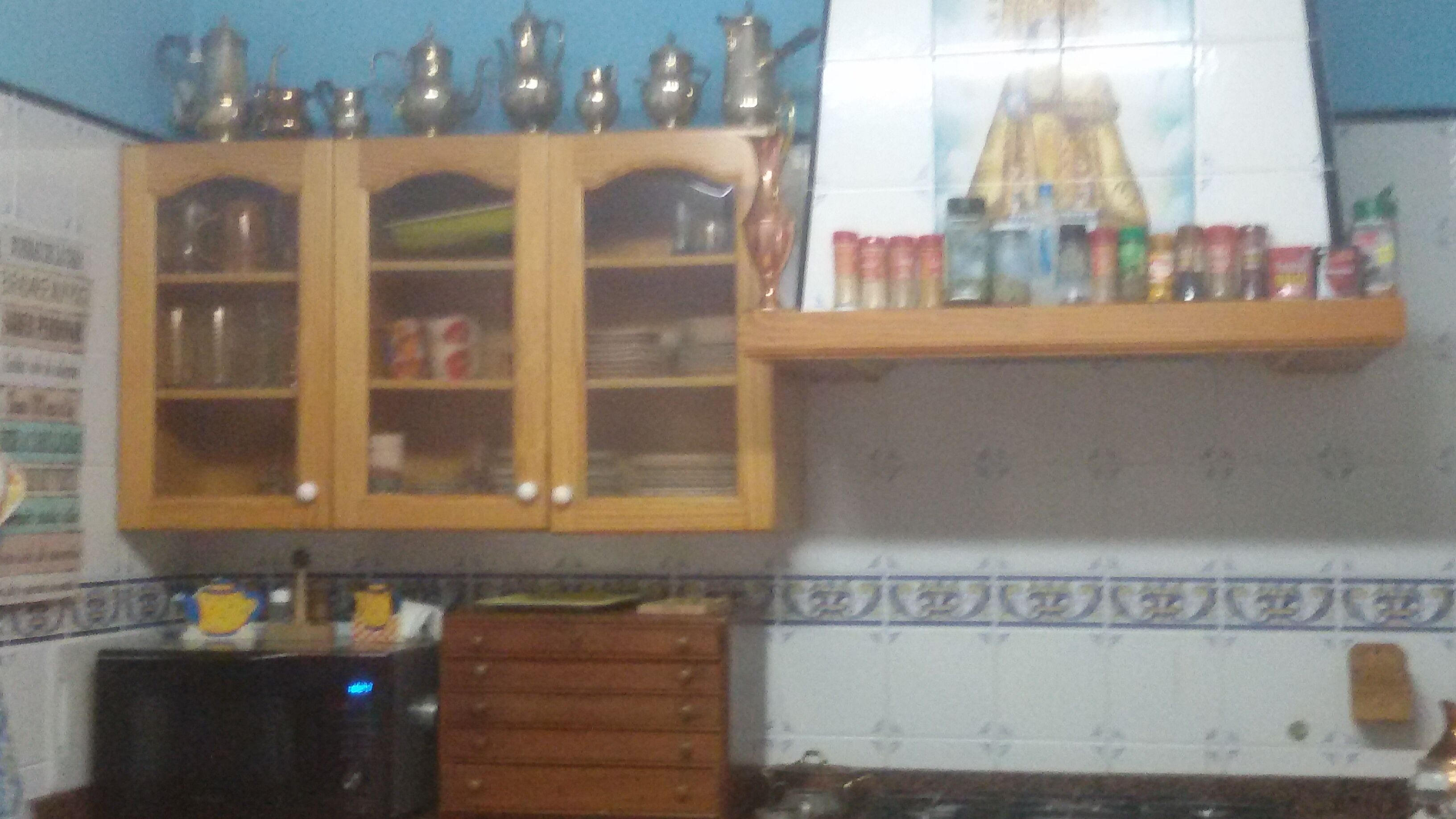 A kitchen with wooden cabinets, a microwave, and a shelf with various items.