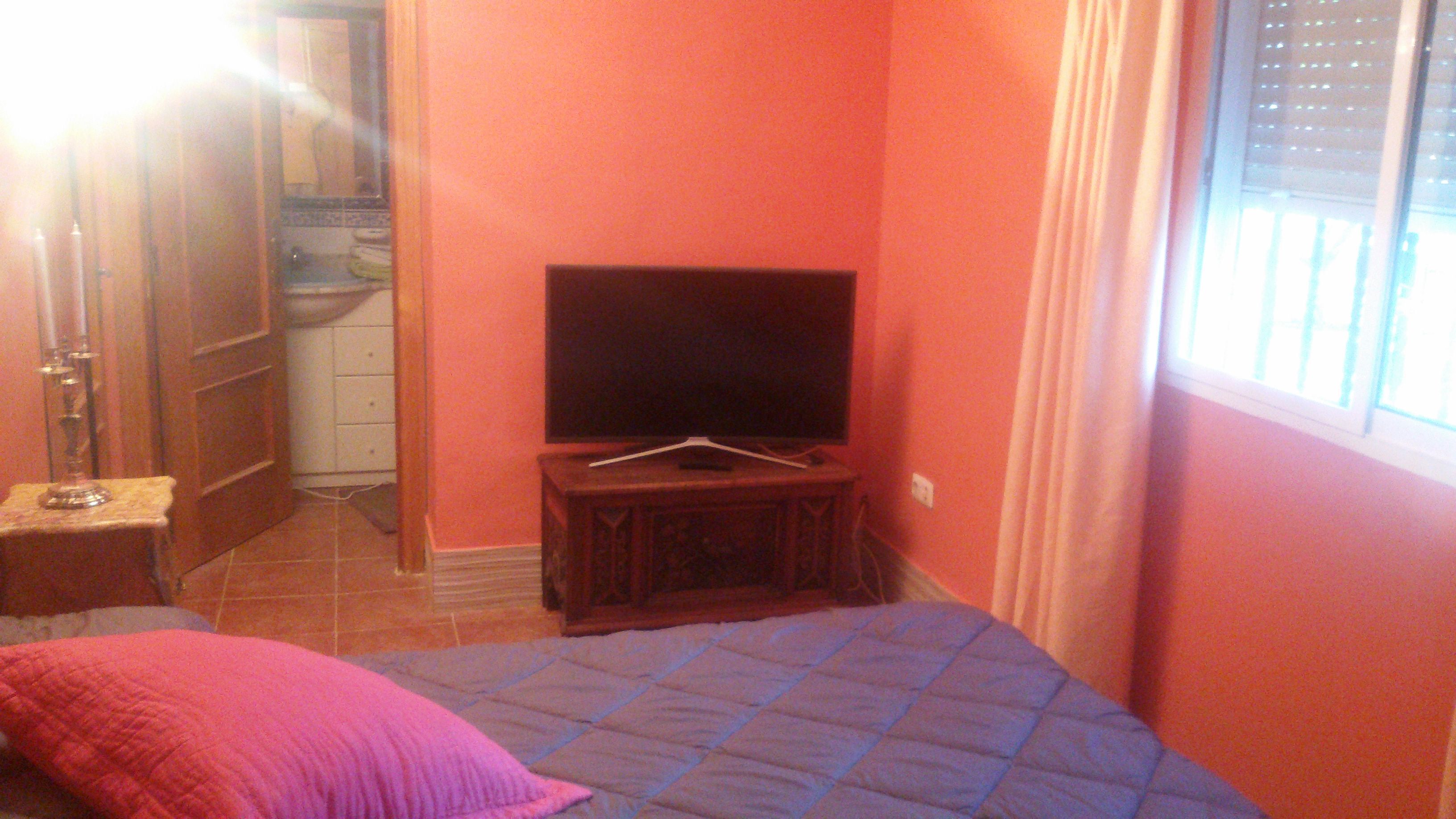 A bedroom with a bed, a television on a stand, a small table, and a window with curtains.