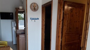 A kitchen with wooden cabinets, a clock, and a door leading to another room. - VILLA GELSOMINO IMMERSED IN THE NATURE SALENTO S. M.DI LEUCA  (corsano)