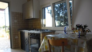 A compact kitchen with a stove, oven, and a dining area with a table and chairs. - VILLA GELSOMINO IMMERSED IN THE NATURE SALENTO S. M.DI LEUCA  (corsano)