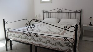 A single bed with a metal frame, white bedding, and a patterned bedspread. There is a nightstand with a lamp on it, and a window above the bed. - VILLA GELSOMINO IMMERSED IN THE NATURE SALENTO S. M.DI LEUCA  (corsano)