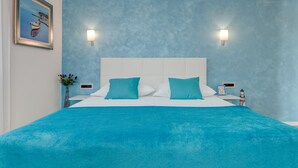 Un dormitorio con una cama grande, dos lámparas de pared, un cuadro enmarcado, una mesita de noche y un pequeño objeto decorativo.