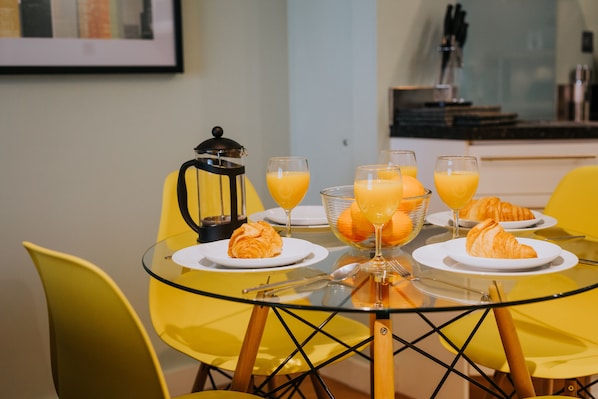 Une table de petit-déjeuner avec des croissants, du jus d’orange et une cafetière.