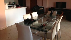 A dining area with a glass table and white chairs, a kitchen in the background, and a TV on a stand. - House with garden, gazebo, barbecue, pizza oven, and a view of Isola Cirella (Diamante)
