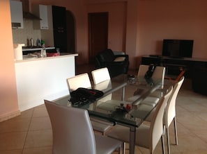 Relax in this stylish living space with a glass dining table, comfortable sofa, and modern kitchen area.
