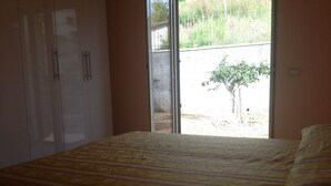 A bedroom with a bed, a wardrobe, and a sliding glass door leading to an outdoor area with a small tree. - House with garden, gazebo, barbecue, pizza oven, and a view of Isola Cirella (Diamante)