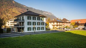 A multi-story building with a flat roof and green shutters, located in a mountainous area with a clear sky. - Spacious and central apartment with terrace (Matten bei Interlaken)