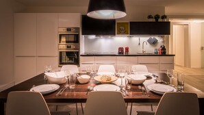 A modern kitchen with built-in appliances, a dining area with a wooden table set for four, and a black pendant light above. - Spacious and central apartment with terrace (Matten bei Interlaken)