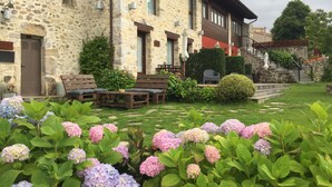 Un edificio de piedra con un jardín delantero, mesas al aire libre y una escalera que lleva al segundo piso.