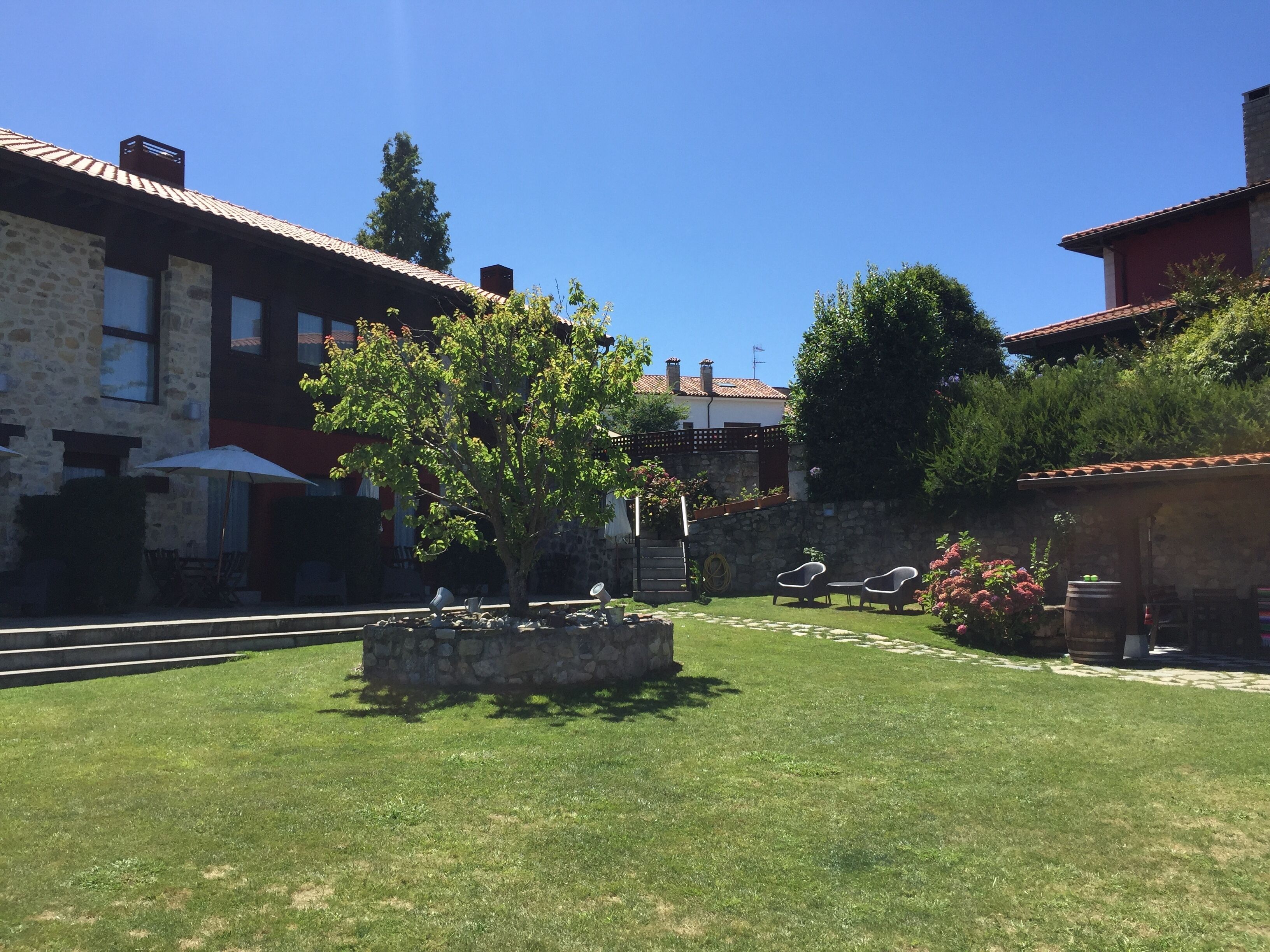 A courtyard with stone buildings, a tree, outdoor furniture, and a clear blue sky.