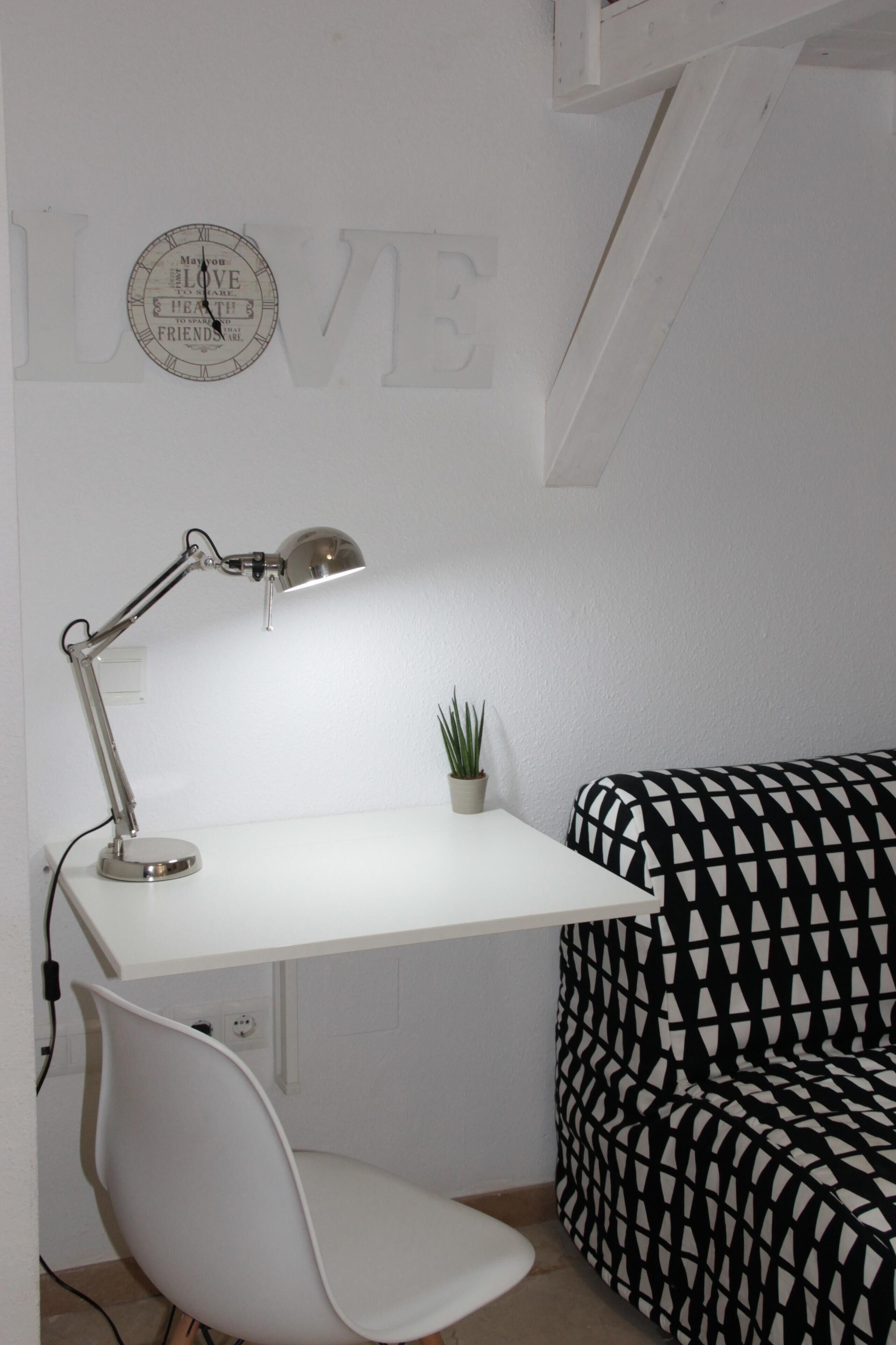 A white desk with a lamp, a small potted plant, and a black and white patterned sofa.
