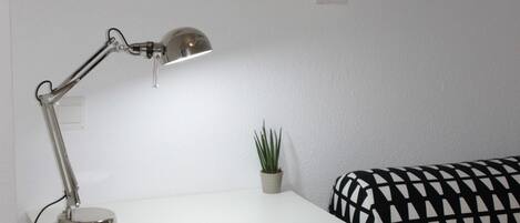 A white desk with a lamp, a small potted plant, and a black and white patterned sofa.