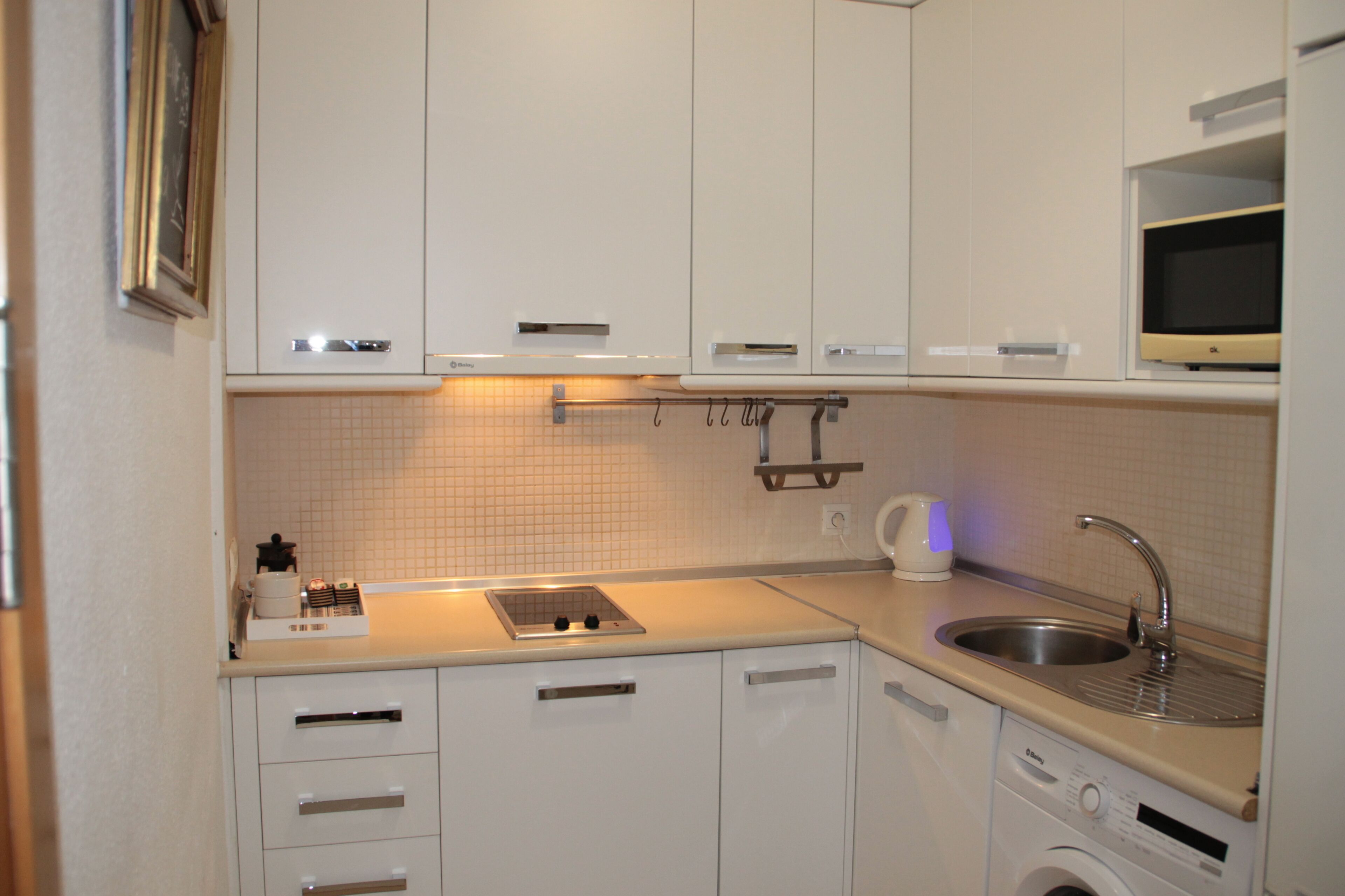 A compact kitchen with white cabinets, a built-in microwave, a sink, and a washing machine.