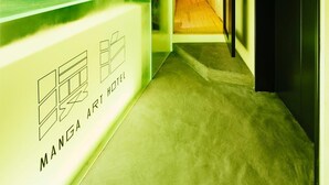 A reception area with a reception desk labeled "Manga Art Hotel," a hallway leading to a room, and a ceiling with exposed ductwork. - MANGA ART HOTEL, TOKYO - Hostel (Tokyo)